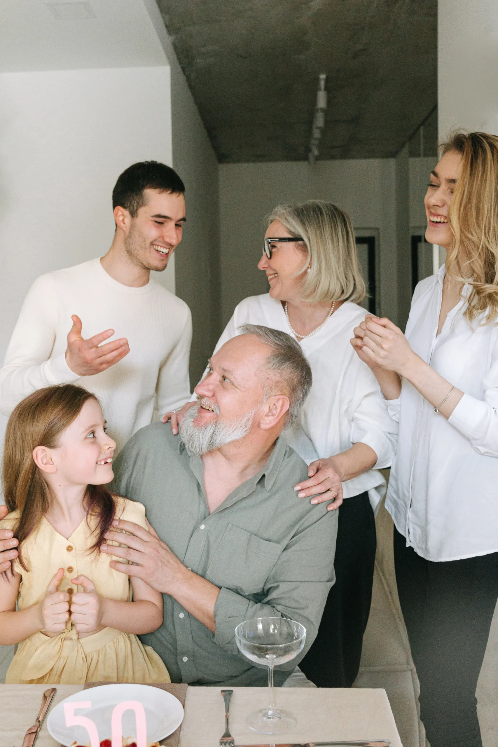Five members of a family, spanning three generations, in shared embrace, smiles and laughter to celebrate one's 50th birthday.